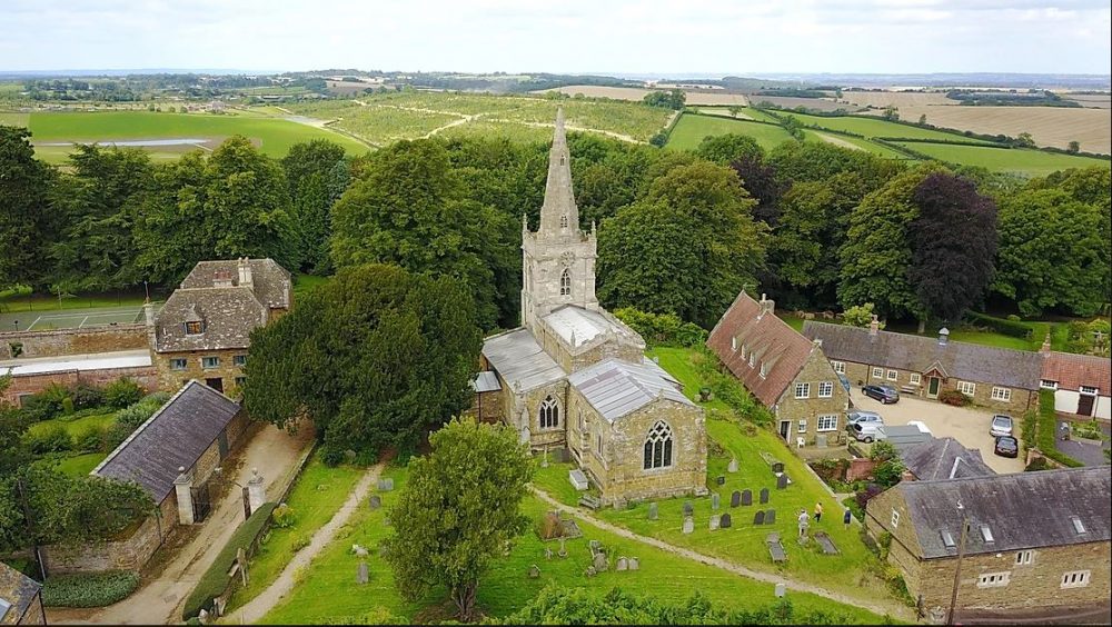 Aerial view of church with steeple, with churchyard, houses and far views