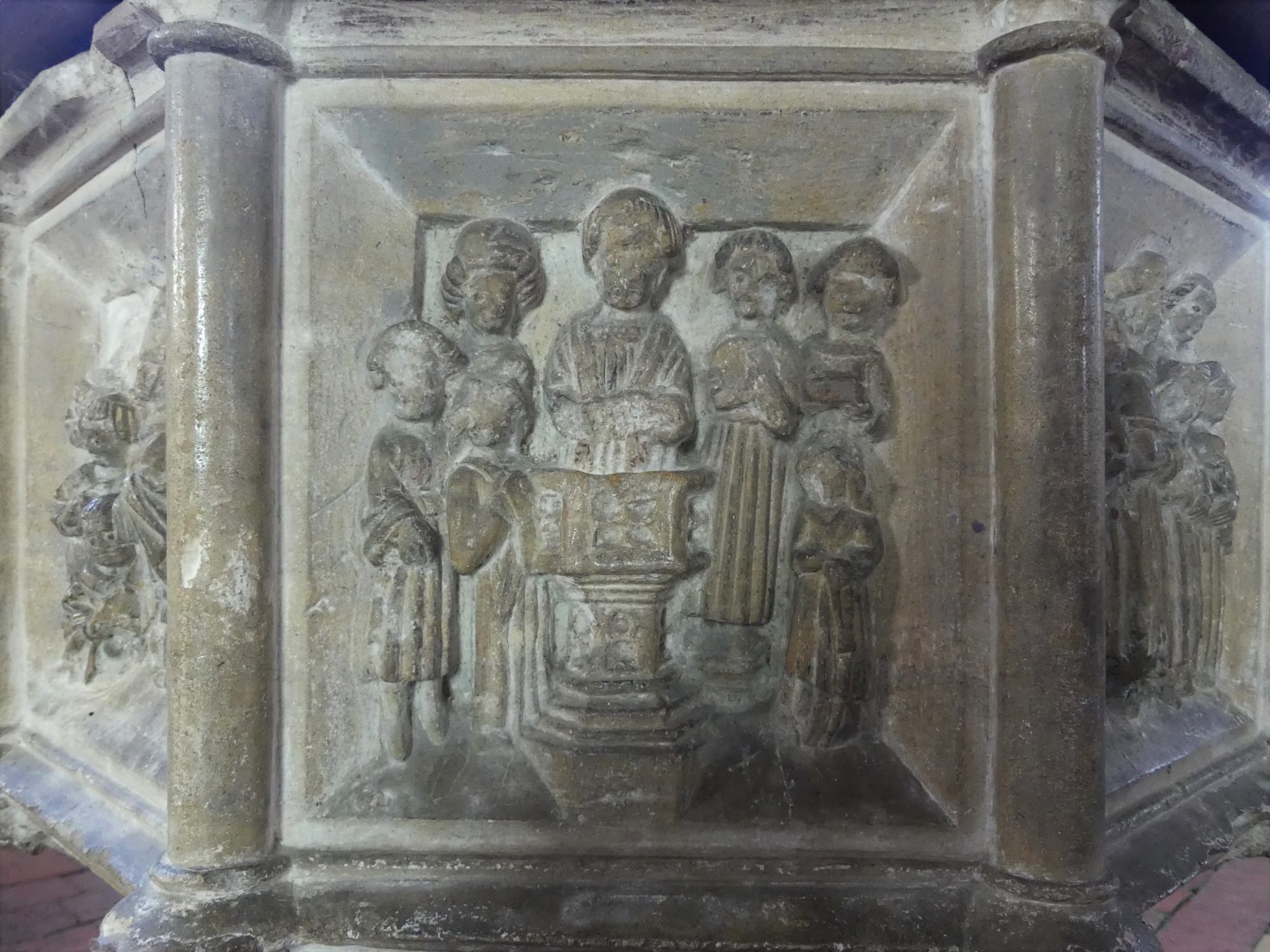 A panel from a carved font showing a baby being baptised