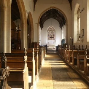 View inside a warm sunlight church with a yellow brick and tile floor and carved pews.