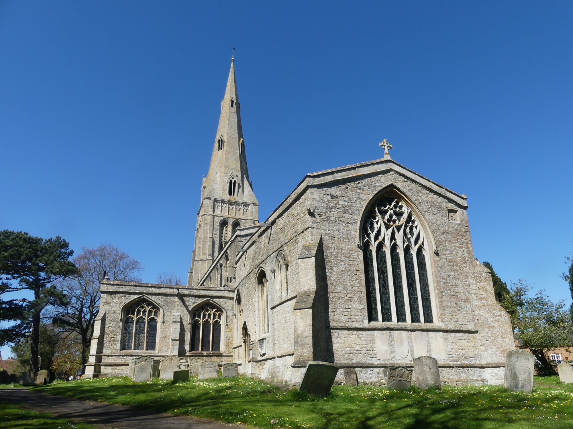 The exterior of St John, Keyston, a large stone church with a towering, narrow spire