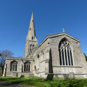 The exterior of St John, Keyston, a large stone church with a towering, narrow spire