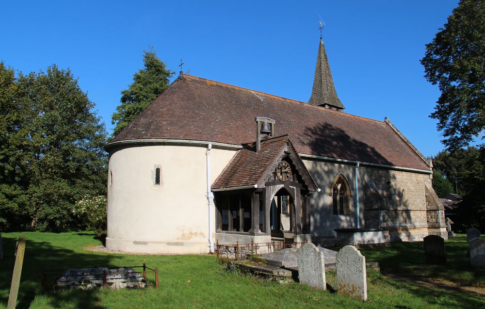 The exterior of a small church with a domed apse and a wodden proch with a clock