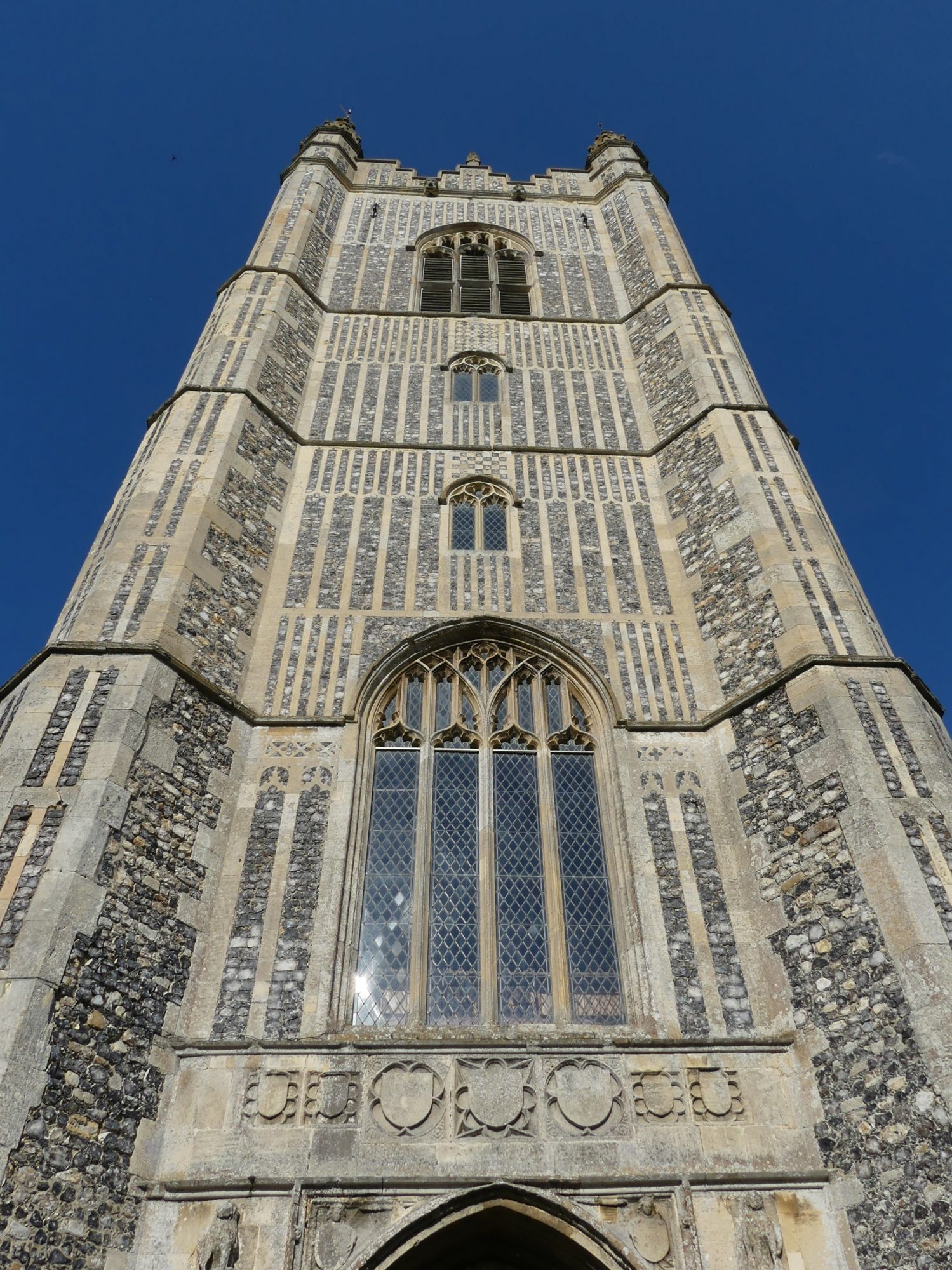 An incredibly tall flint tower, show from ground level. The tower is covered in decorative stone work and flint set in regular patterns