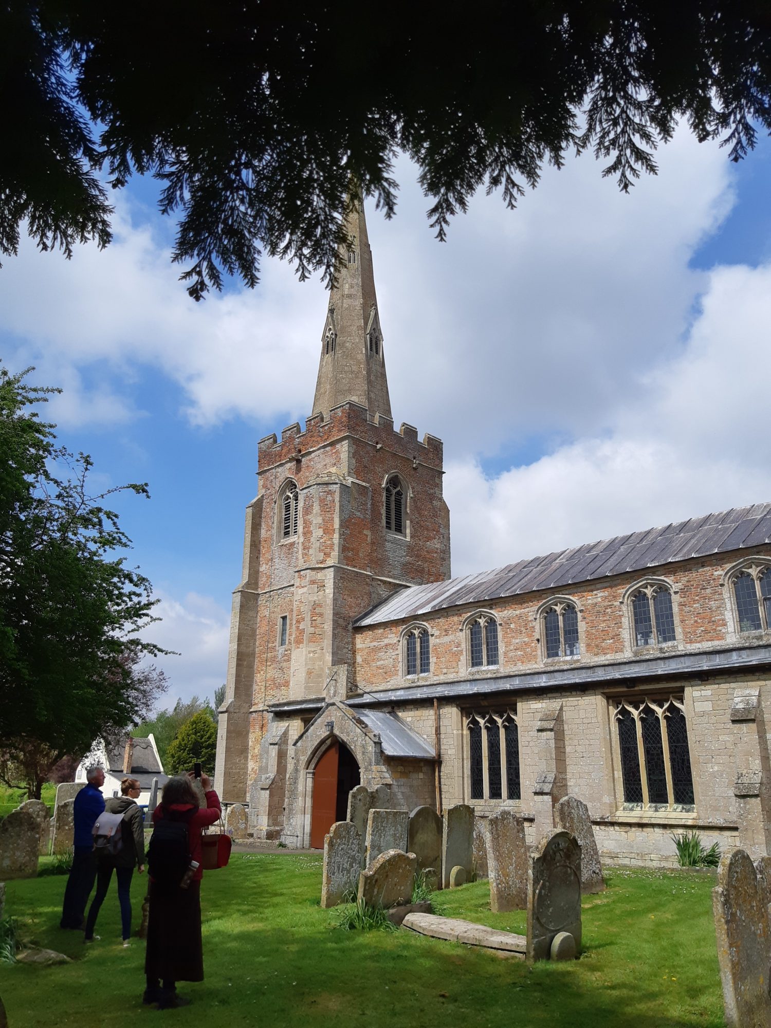 A church made of stone and red brick with a tower topped by a narrow steeple