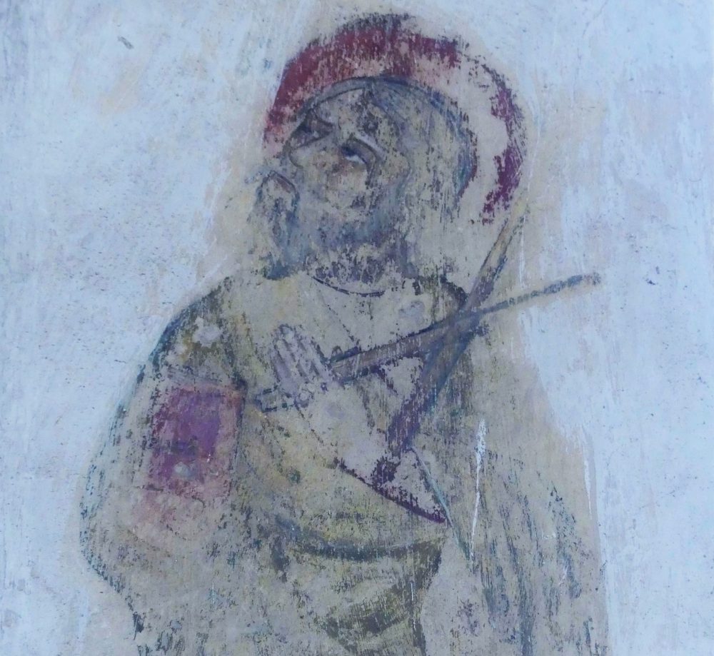 A medieval painting showing St Andrew holding a cross, the painting had red and black pigment showing against a white wall