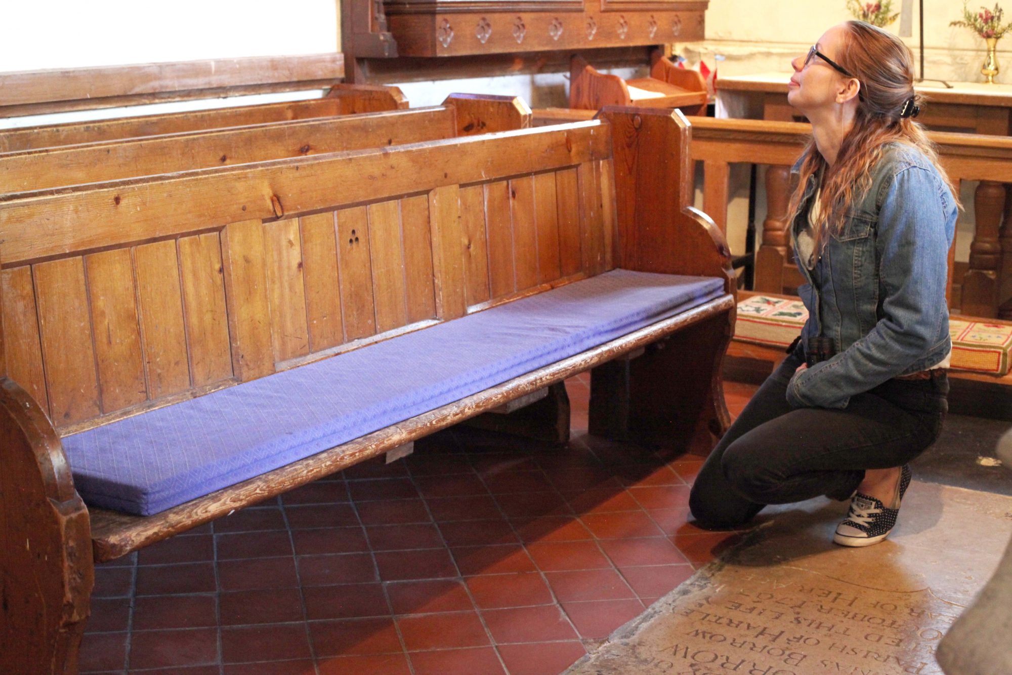 A young woman kneeling by a pew and looking for signs of bats