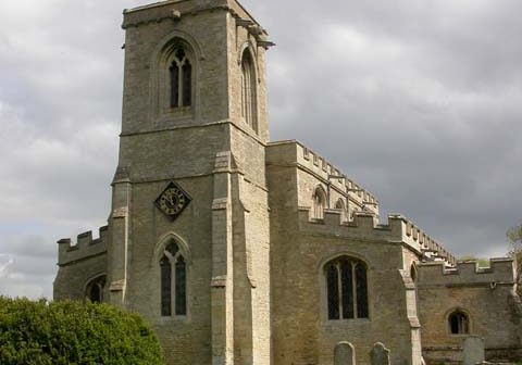 The exterior of a honey coloured stone church with tower and s amll steeple