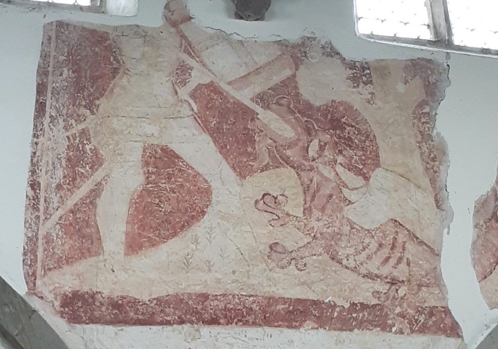 A medieval wall painting in tones of red showing the lower half of St George spearing the mouth of a small dragon