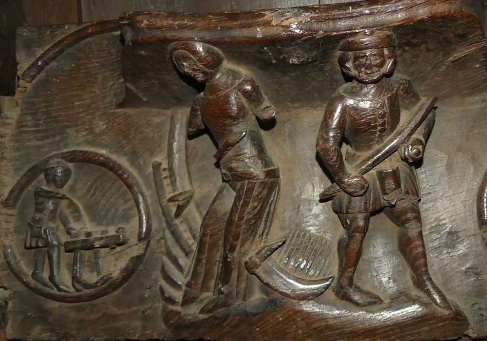 A medieval carved miserichord showing a man reaping wheat with a scythe alongside another figure