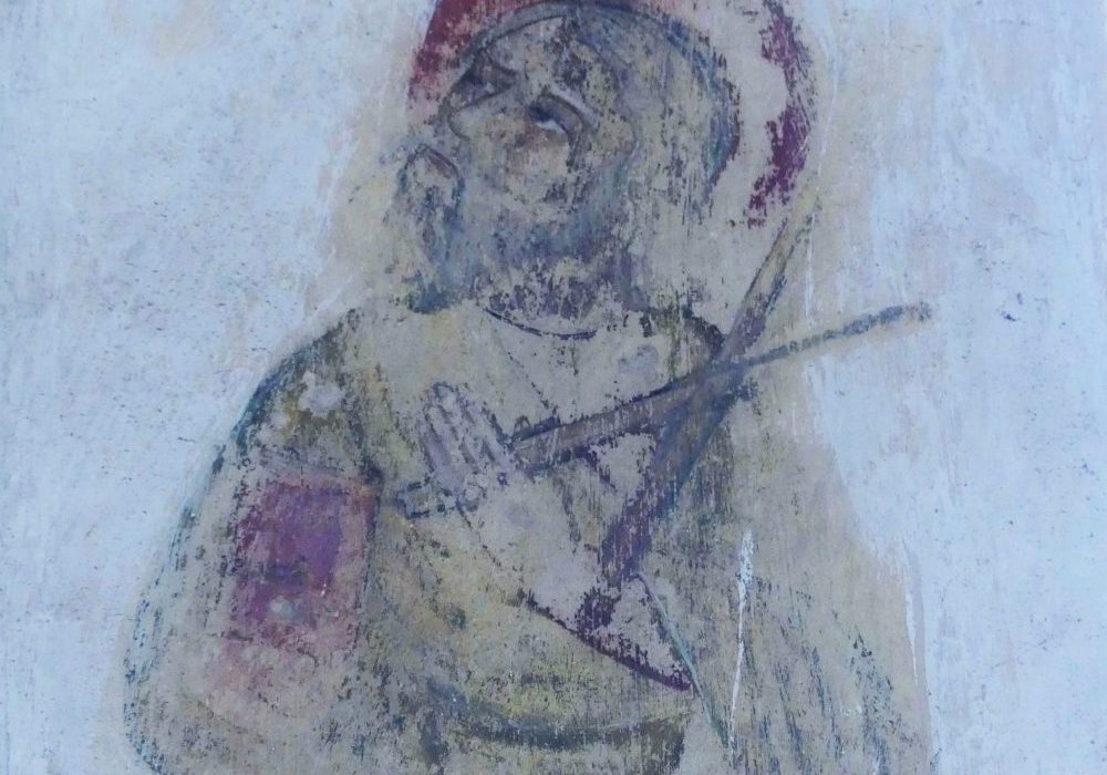 A medieval painting showing St Andrew holding a cross, the painting had red and black pigment showing against a white wall