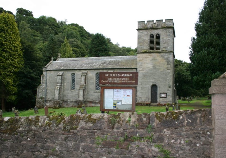 Church with bell tower, surrounded by trees, with sign and a few people in churchyard