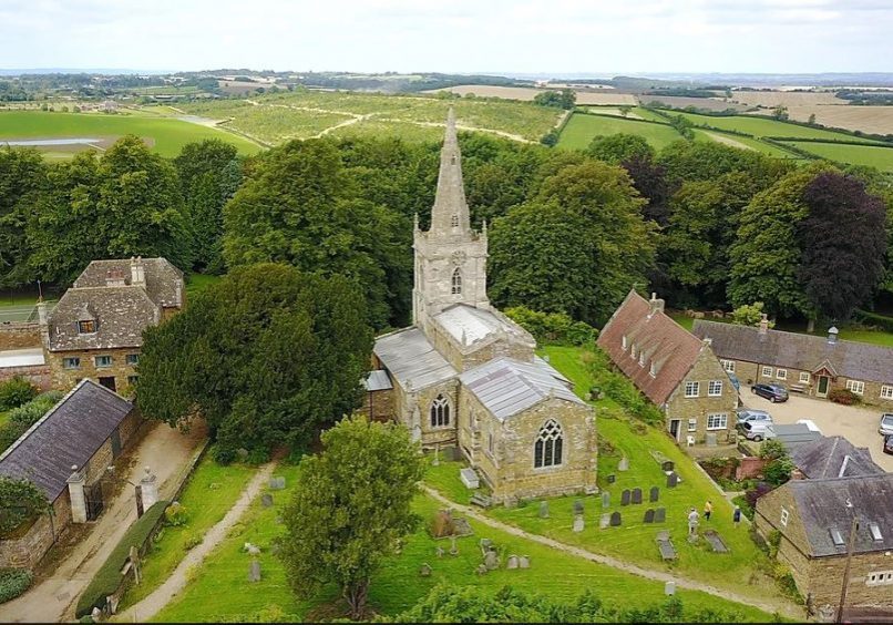 Aerial view of church with steeple, with churchyard, houses and far views