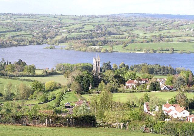 Looking down on church tower beside a lake with fields and houses
