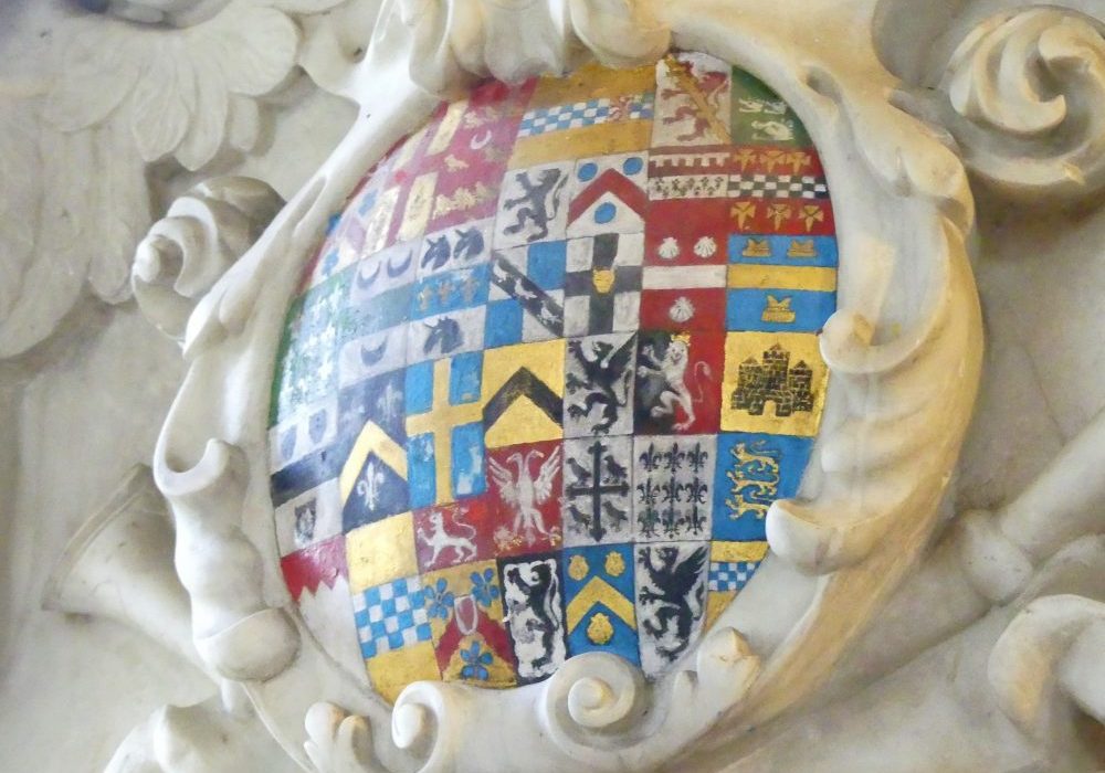 A circular marble surround filled with approximately 40 tiny coats of arms, in red, blue, gold, black and white, showing animals, birds, crosses, chevrons and squares