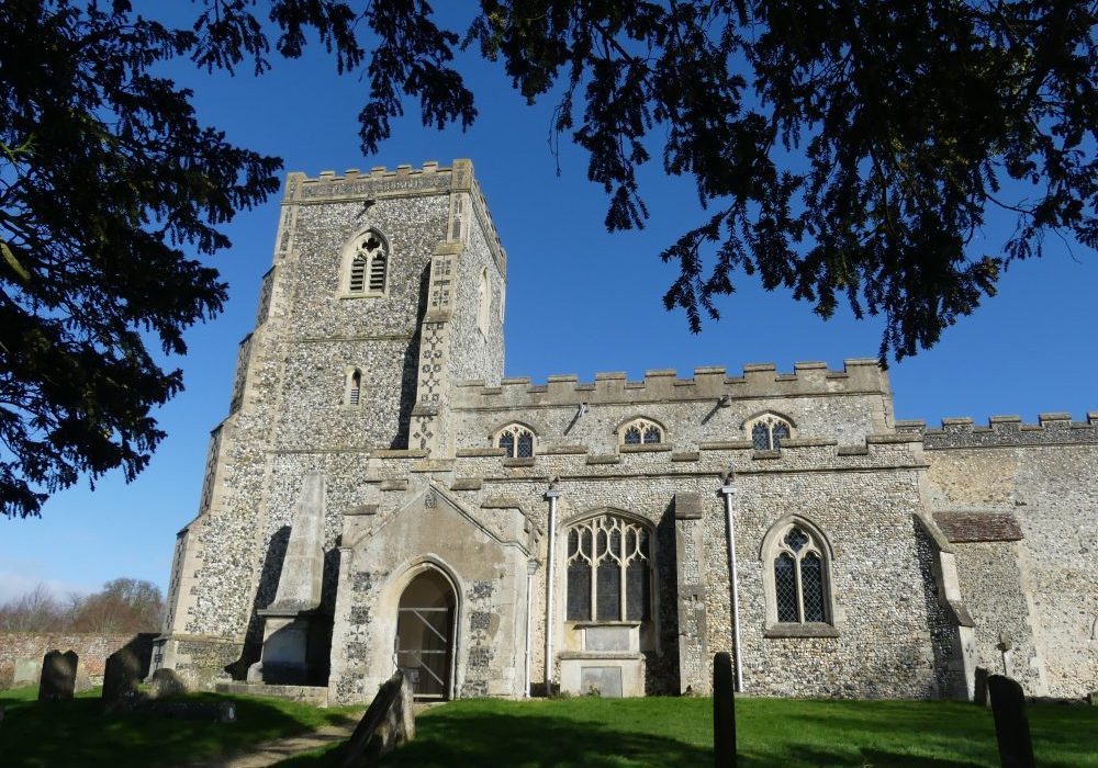 A flint church with a low, solid looking tower, the image is framed by yew trees