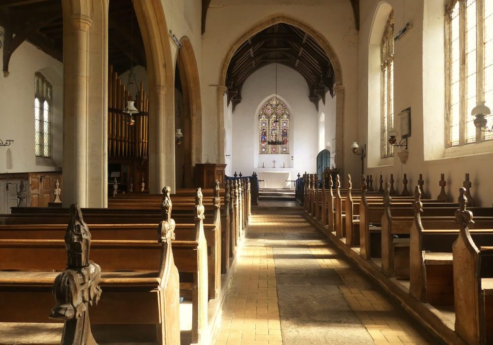 View inside a warm sunlight church with a yellow brick and tile floor and carved pews.