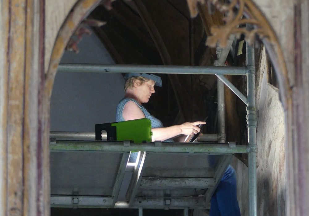 Conservator sitting on a scaffold examining a wall painting
