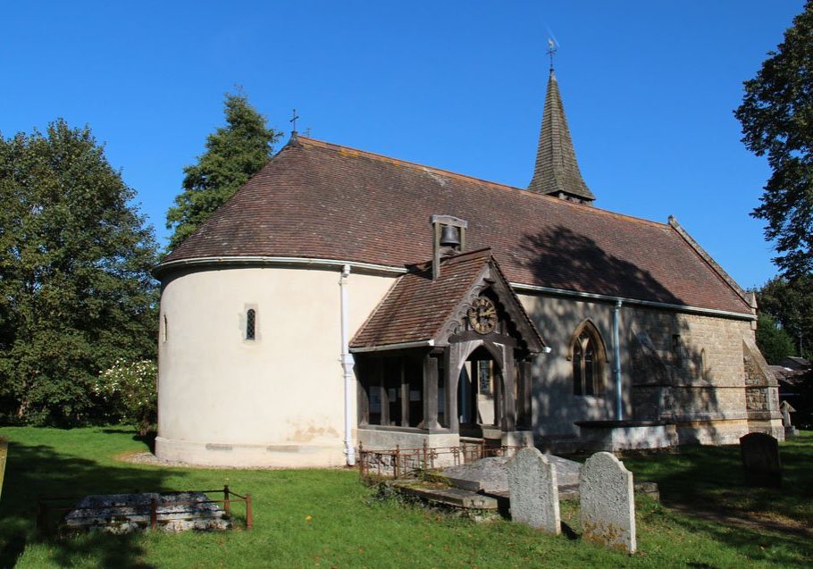 The exterior of a small church with a domed apse and a wodden proch with a clock