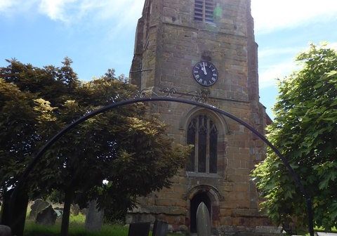 Church tower with clock and ironwork arch over gate