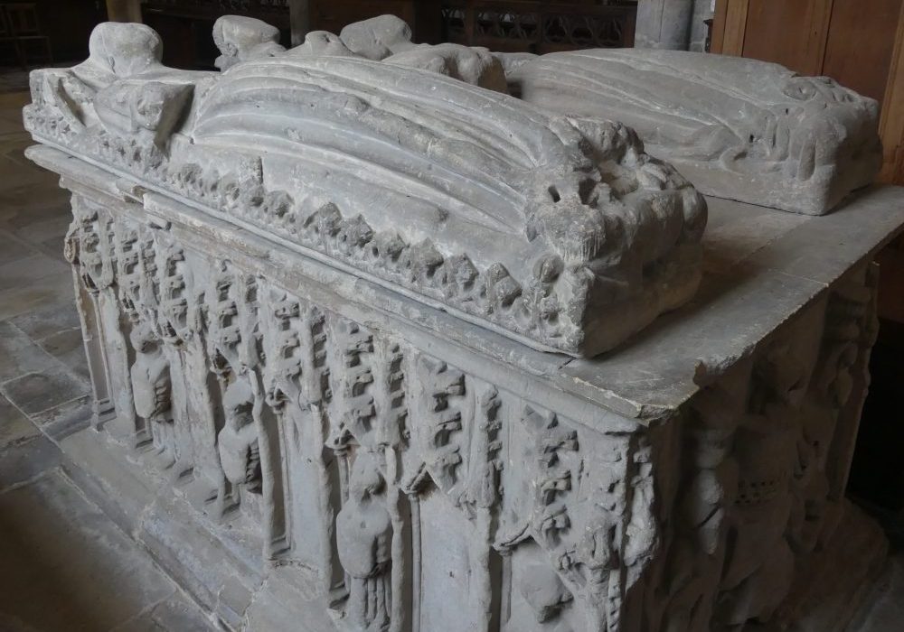 A tall, stone, table tomb with niches and figures around the side and two carved lying effigies on top