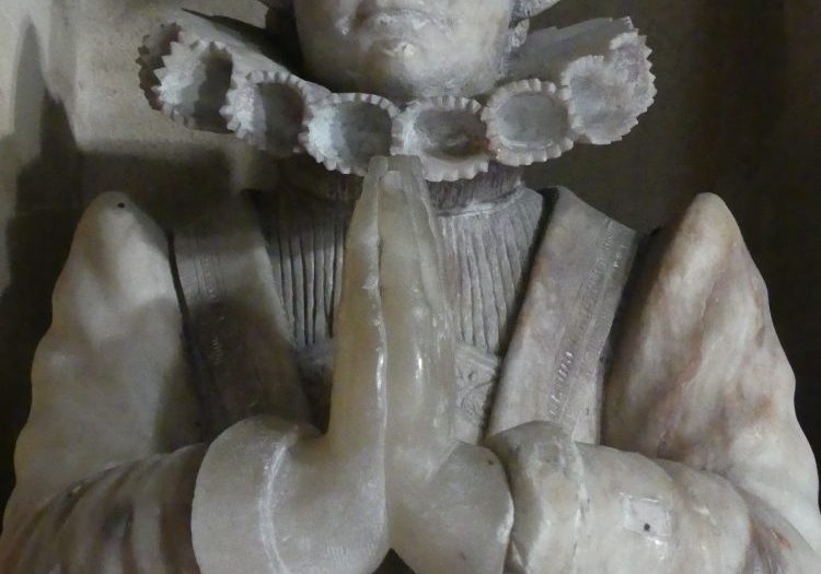 An alabaster statue of a woman wearing a ruff and tudor gown, praying with clasped hands
