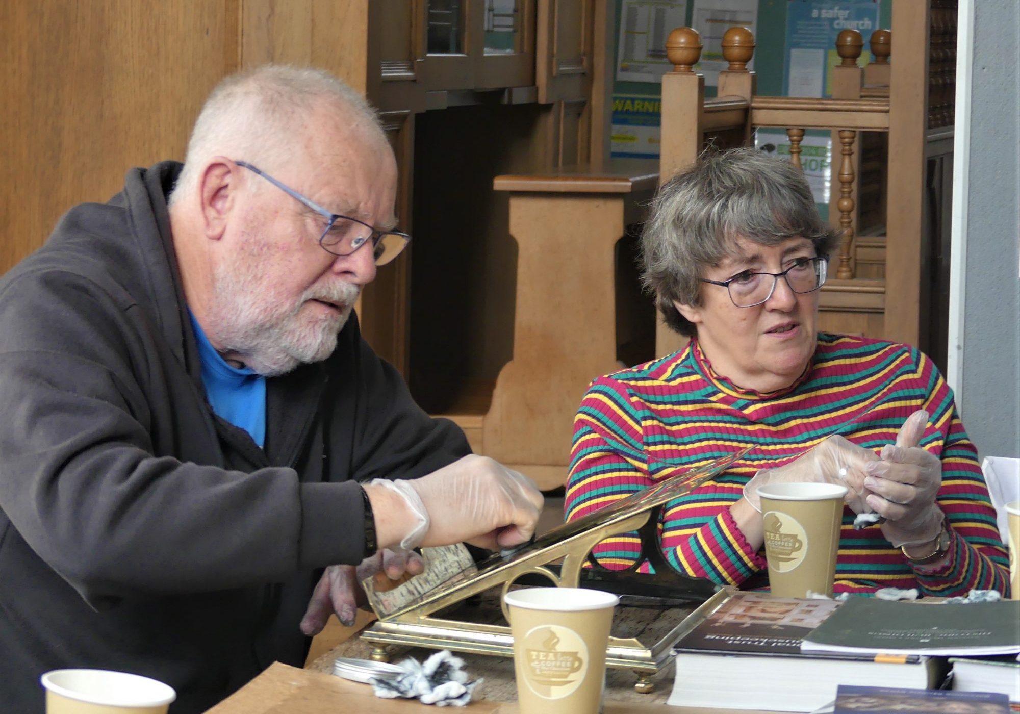 Two people seated at a table cleaning brassware from the church