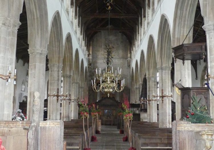 View down the aisle facing west, the church has a red tiled floor and six large arches in each arcade, topped by a clerestory
