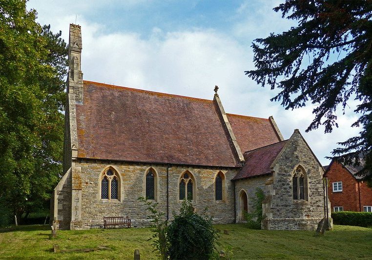 Stone church with red tiled roof with door in south transept and bench