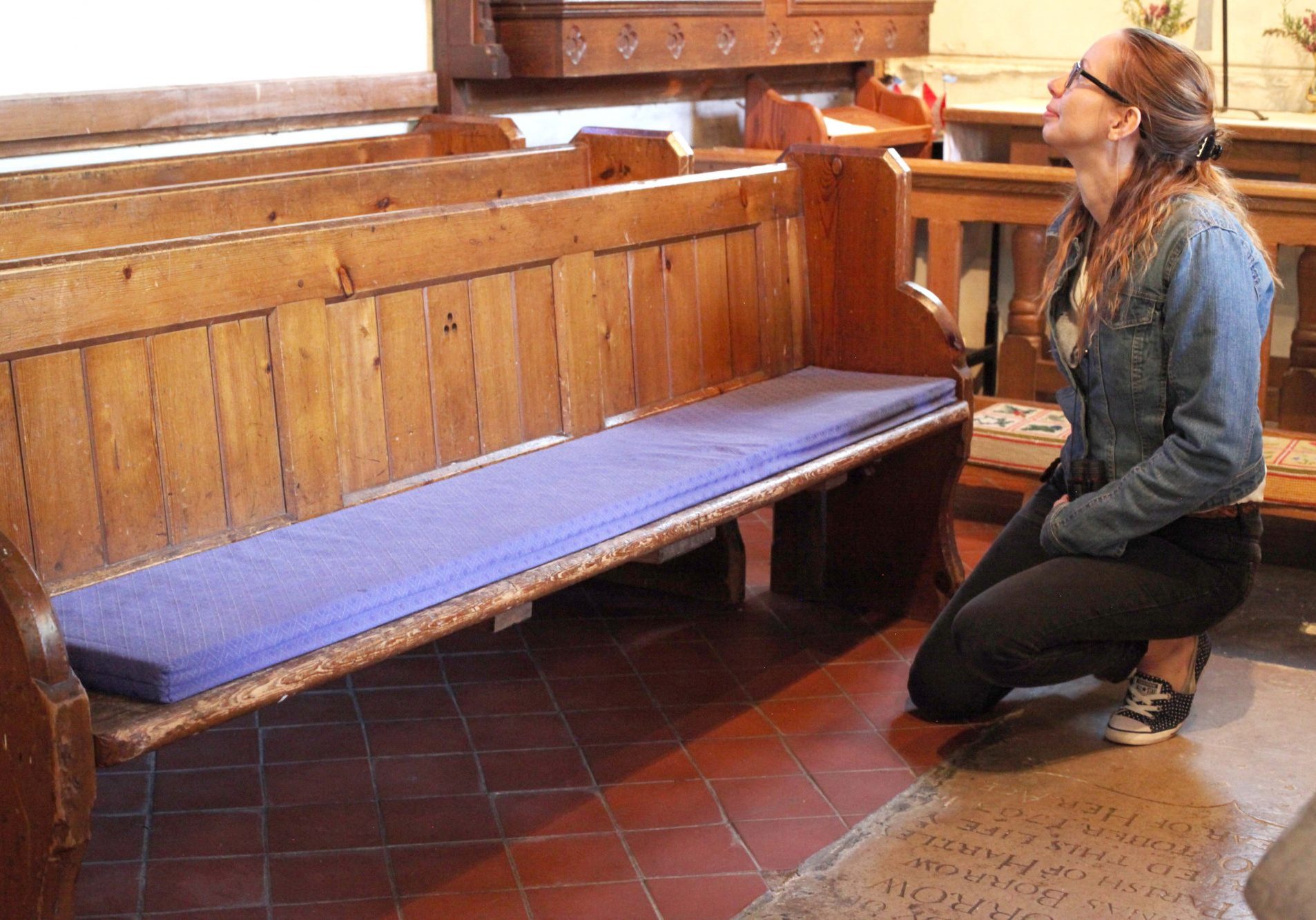 A young woman kneeling by a pew and looking for signs of bats